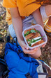 © zhukovvvlad - The boy takes out a lunch box and prepares to eat on a hike. food on the street. hiking with a child.