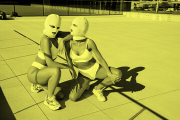 Two beautiful sexy women in green underwear. Models wearing bandit balaclava mask. Hot seductive female in nice lingerie posing in the street at sunny day, blue sky. Crime and violence. Retro colour