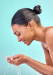 © peopleimages.com - Woman washing face, hands and water drops for skincare, hygiene and beauty or dermatology in studio. Model with palm and liquid for facial wellness, natural and cosmetic cleaning on blue background