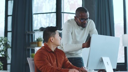 Aufkleber - Two men are seated at a desk, focused on a computer screen in front of them. They appear engaged in work or a discussion, their expressions concentrated.
