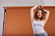 © Flamingo Images - Smiling young redheaded woman dancing against an orange backdrop