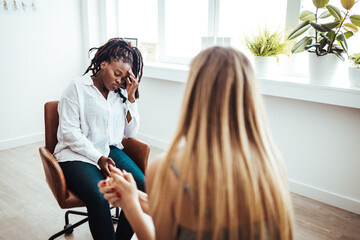 Wall Mural - Psychotherapy session, woman talking to his psychologist in the studio. Young woman visiting therapist counselor. Girl feeling depressed, unhappy and hopeless, needs assistance. 