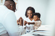 © Dragana Gordic - A happy toddler boy sits in his mother' lap at the pediatrician. He plays patacake with a doctor. Doctor giving prescription to african american mother with baby son at clinic.