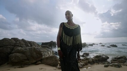 Wall Mural - Trans multiracial model poses at scenic seaside location faces camera. Non-binary black person in outrageous gown stands with their back to camera at rocky ocean beach. Male gay in posh dress by sea