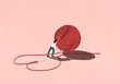 © fStop - Woman pushing large ball of red string forming heart-shape on pink background