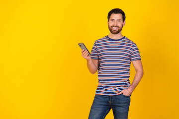 Poster - Photo of clever man with beard dressed striped t-shirt hold smartphone near promotion empty space isolated on yellow color background