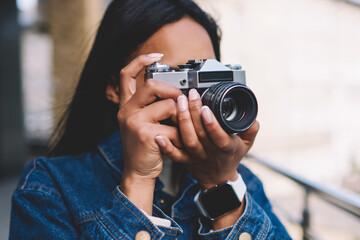 young dark skinned hipster girl in jeans jacket spending time on hobby taking pictures on city stree