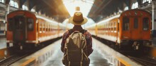 A Traveler With A Hat And Backpack Stands At The Station Platform, Facing Away From The Camera. The Photo Was Taken In Low Light, Creating An Atmosphere Of Mystery And Adventure. It Was Done In The St