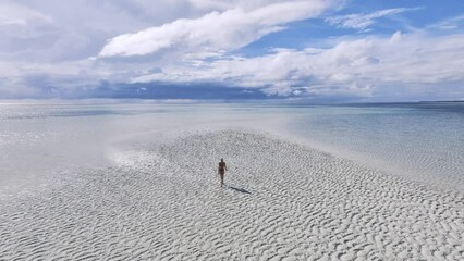 Canvas Print - Aerial view of young woman on the sandbank in ocean, white sand, blue sea in low tide at sunny summer day in Zanzibar island. Top view of girl, sand spit, bay, sky with clouds reflected in clear water