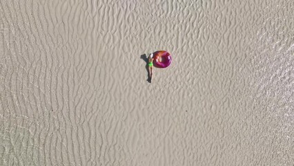 Wall Mural - Aerial view of lying sporty slim woman with swimming ring, sandy beach in low tide at sunrise in summer in Zanzibar island. Top view of beautiful girl, sandbank, ocean, clear water. Tropical scenery