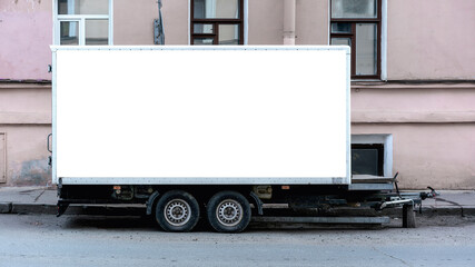 Trailer with blank white billboard parked on urban street, mockup for advertisement. Side view of cargo trailer with space for branding against building facade