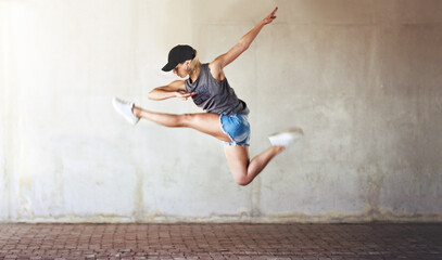 woman, dancing and jump with city wall background or creative workout for hip hop, urban or fitness.