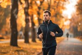 Man jogging through autumn park wearing black jacket with earphones