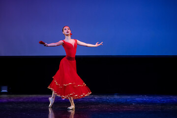 ballerina in a red dress performs a variation from the ballet Don Quixote on the theater stage.