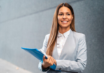 Portrait photo of a smiling female financial advisor standing with a folder with files in her hand.