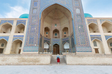 Back view of Young woman at Bukhara, Uzbekistan Mir-i-Arab Madrasa Kalyan minaret and tower. Translation on mosque: 