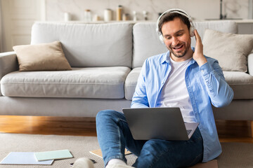 Poster - A man is seated on the floor, wearing headphones and concentrating on his laptop screen. He appears focused and engaged in his work or entertainment. The setting is indoors, with minimalistic decor.