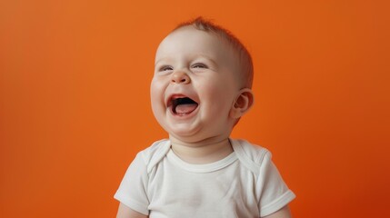 A happy baby giggles gleefully while alone against a soft pastel orange backdrop