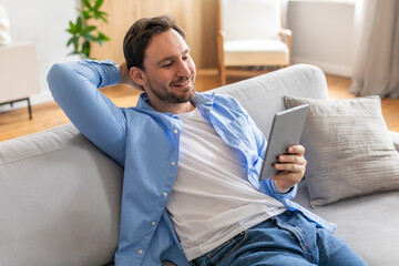 Poster - A man is casually sitting on a couch, engrossed in using a tablet device. He appears focused as he interacts with the screen, showcasing modern technology in everyday life.