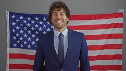 Canvas Print - Smiling professional man in suit stands before an american flag in a corporate setting, suggesting a patriotic theme.