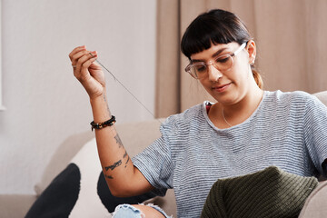 woman, hands and embroidery on sofa for stitching fabric patch with needle on sweater at home. femal