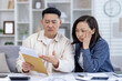 © Liubomir - A worried couple sits at home, reading a letter with bad news. They look distressed as they discuss the contents of the envelope.