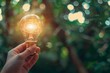 © JK_kyoto - A closeup of a hand holding a light bulb bright with light on a green nature background