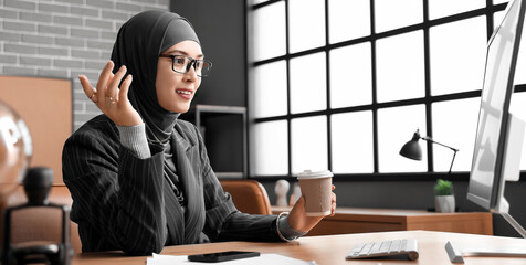 Canvas Print - Muslim businesswoman with cup of coffee working at table in office