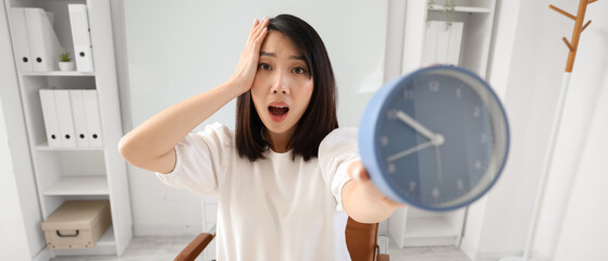 Canvas Print - Shocked Asian woman with alarm clock in office