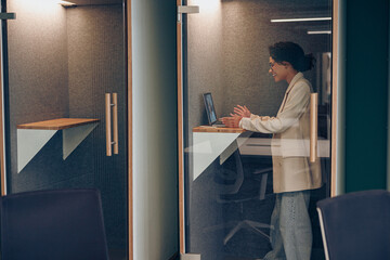 Wall Mural - Young female freelancer talking with colleague via video call while sitting in modern coworking