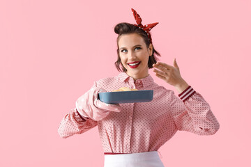 Poster - Beautiful young happy pin-up housewife holding baking tray with croissant on pink background