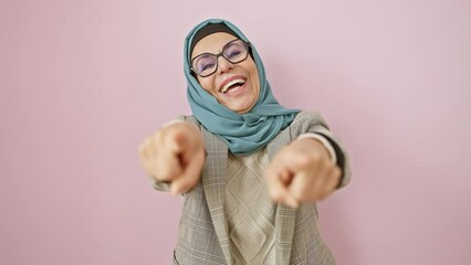 Wall Mural - Cheerful middle age hispanic woman in hijab, pointing at you through the camera lens over an isolated pink background, signifying a pick for something positive!