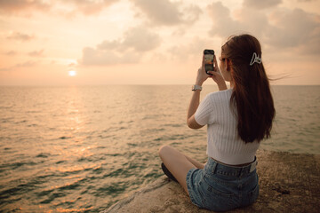 Asian girl taking pictures of the sunset at the beach