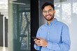 © Tetiana - Confident young man in the office holding a smartphone and smiling