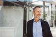 © contrastwerkstatt - Confident senior businessman standing outside a modern office building, looking thoughtful and reflective. Professional and successful executive in an urban environment.