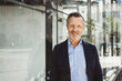 © contrastwerkstatt - Mature businessman in formal attire standing outdoors near a modern glass building, exuding confidence and professionalism.