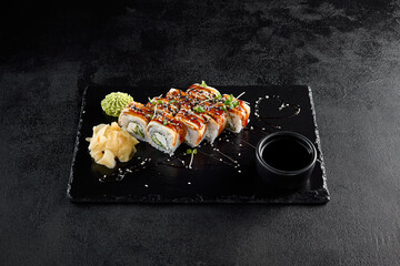 Sticker - Canada roll with eel and unagi sauce, presented on a black slate with soy sauce and wasabi