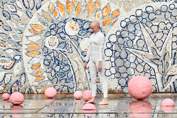 Wall Mural - Young hairless girl ballerina with alopecia in white futuristic suit dancing outdoor among pink spheres on abstract mosaic Soviet background, symbolizes self expression and acceptance of unique beauty