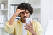 © Liubomir - Frustrated young man looking at smartphone with concern in home office