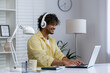 © Liubomir - Young man working from home with headphones on laptop in modern office setup