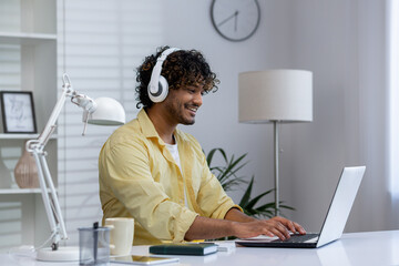 Young man working from home with headphones on laptop in modern office setup