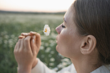Wall Mural - A woman is holding a flower and smelling it. Concept of peace and tranquility, as the woman is enjoying the simple pleasure of smelling a flower in a field. The scene is serene and calming