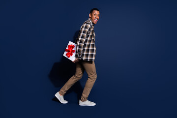 Wall Mural - Full length photo of good mood guy wear checkered shirt walking hiding gift box emtpy space isolated blue color background