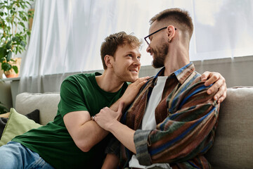 Gay couple creating trendy attire, sitting together on top of a couch in a designer workshop.