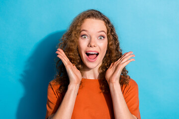 Photo portrait of youth beautiful funny girl with wavy hair wear orange t shirt raised hands up surprised isolated on blue color background