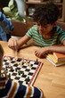 © pressmaster - High angle of pensive boy in striped t-shirt sitting by table in front of his checkmate and thinking of where to move white pawn