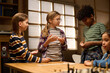 © pressmaster - Youthful boy and girl looking at cute African American boy with domino tiles in hands while standing by table before playing board game