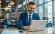 © OLGA - Joyful businessman in a blue suit working on a laptop in a modern office.