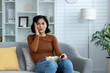 © Tetiana - Scared and worried young woman sitting on sofa at home, holding bowl of popcorn on lap and looking ahead with fear, watching scary movie and news, holding hand to head in shock