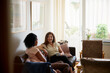 © Johnér - Mature woman having coffee and talking with female friend while sitting on sofa at home